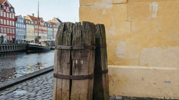 Weathered timber mooring post and yellow lime-washed wall in Copenhagen harbor